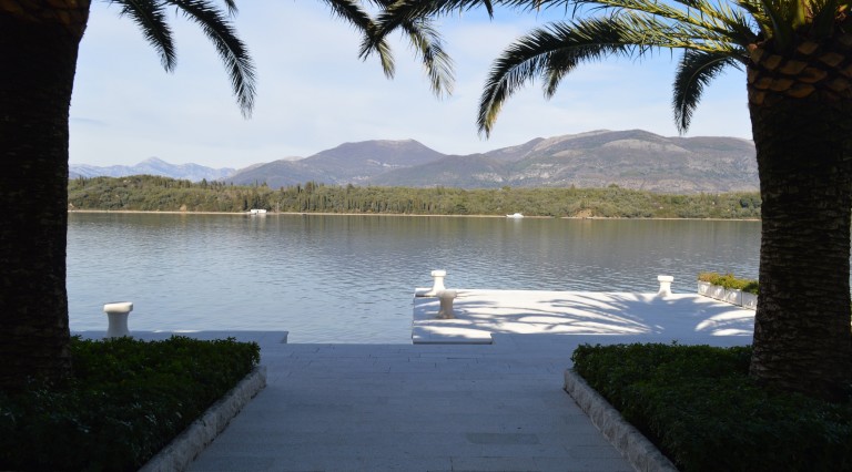 Sea and mountain view from a private villa pier in Tivat, Montenegro: stone terrace, palm trees, and panoramic scenery.