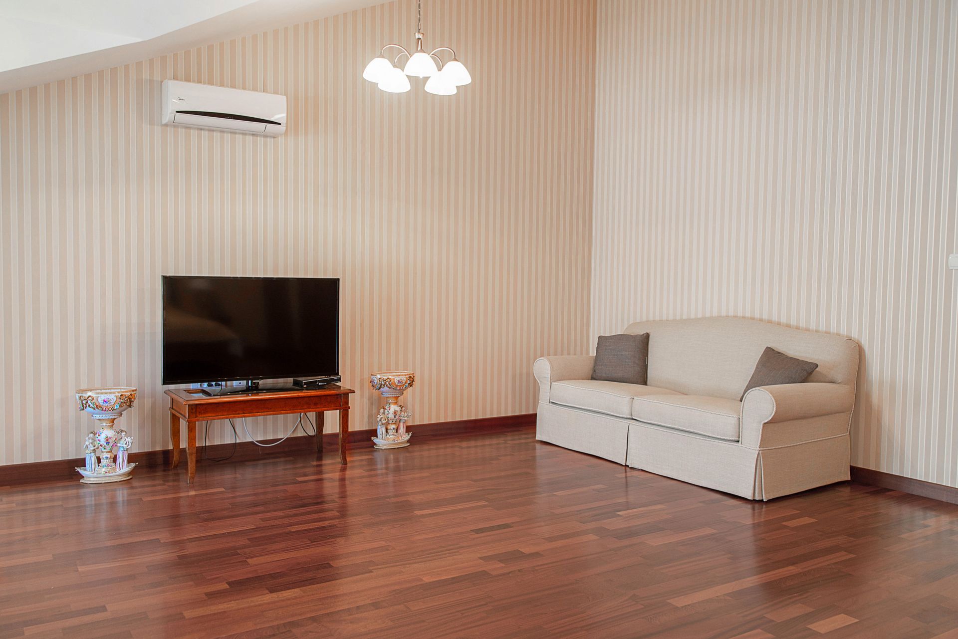 Living room in a townhouse in Lastva, Montenegro: light-colored sofa, TV, parquet floor, air conditioner, and classic decor.