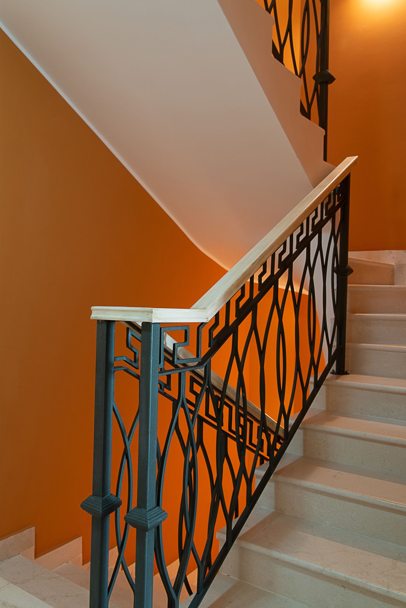 Marble staircase with wrought-iron railings in a townhouse in Lastva, Montenegro: interior with orange walls.
