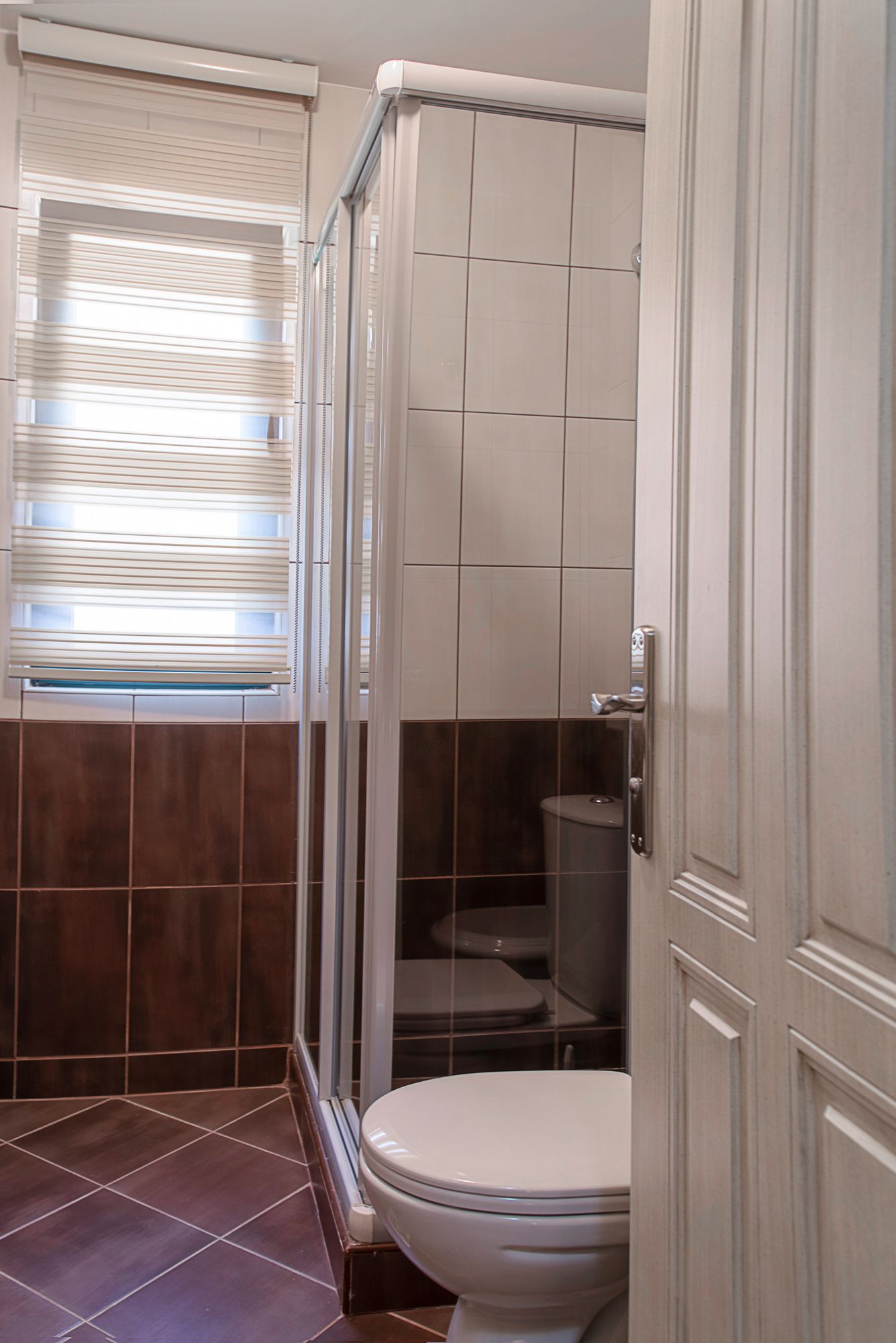 Bathroom in a townhouse in Lastva, Montenegro: shower cabin, light-colored tiles, and a window with blinds.