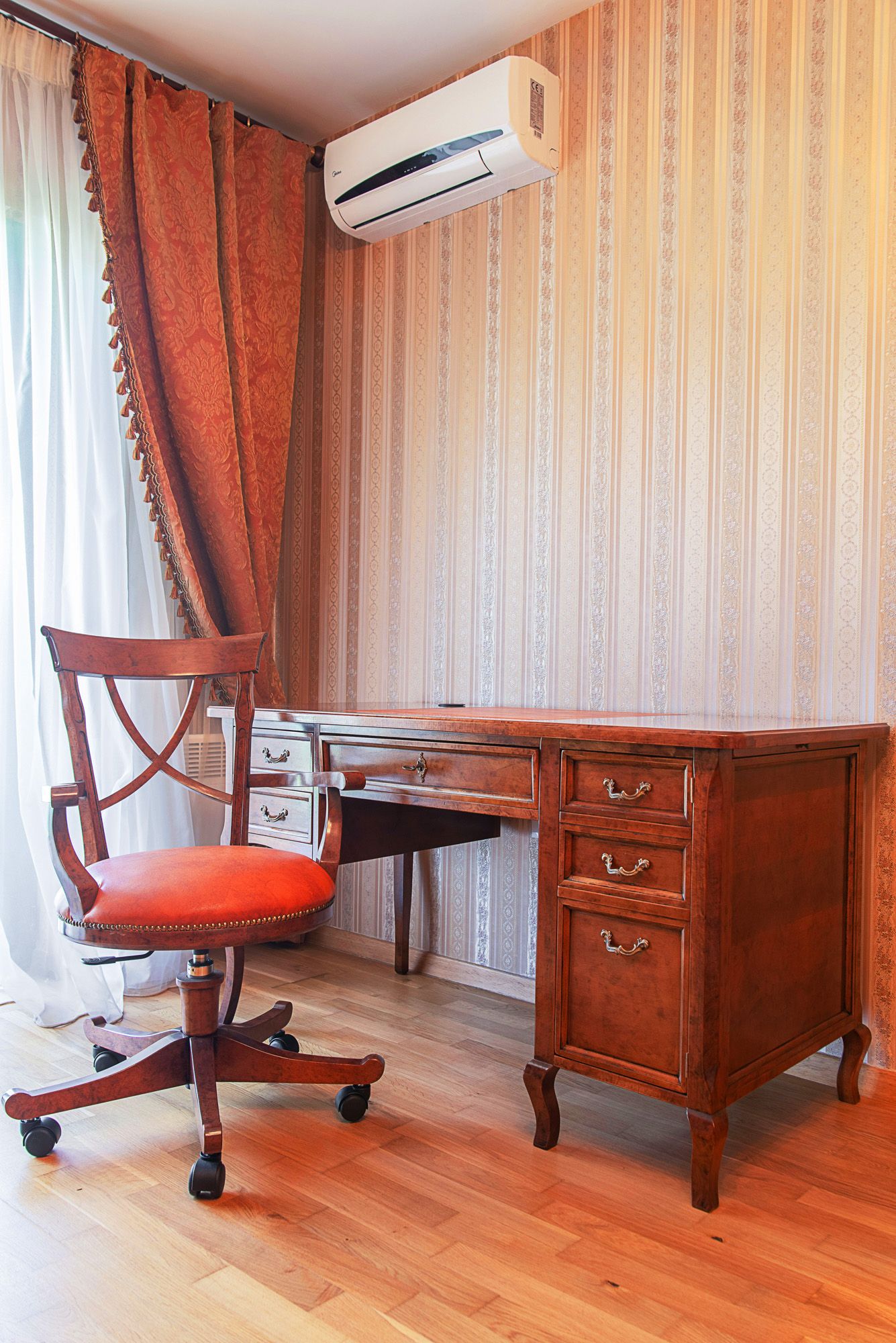 Home office in a townhouse in Lastva, Montenegro: an antique wooden desk, armchair, and air conditioner in the interior.