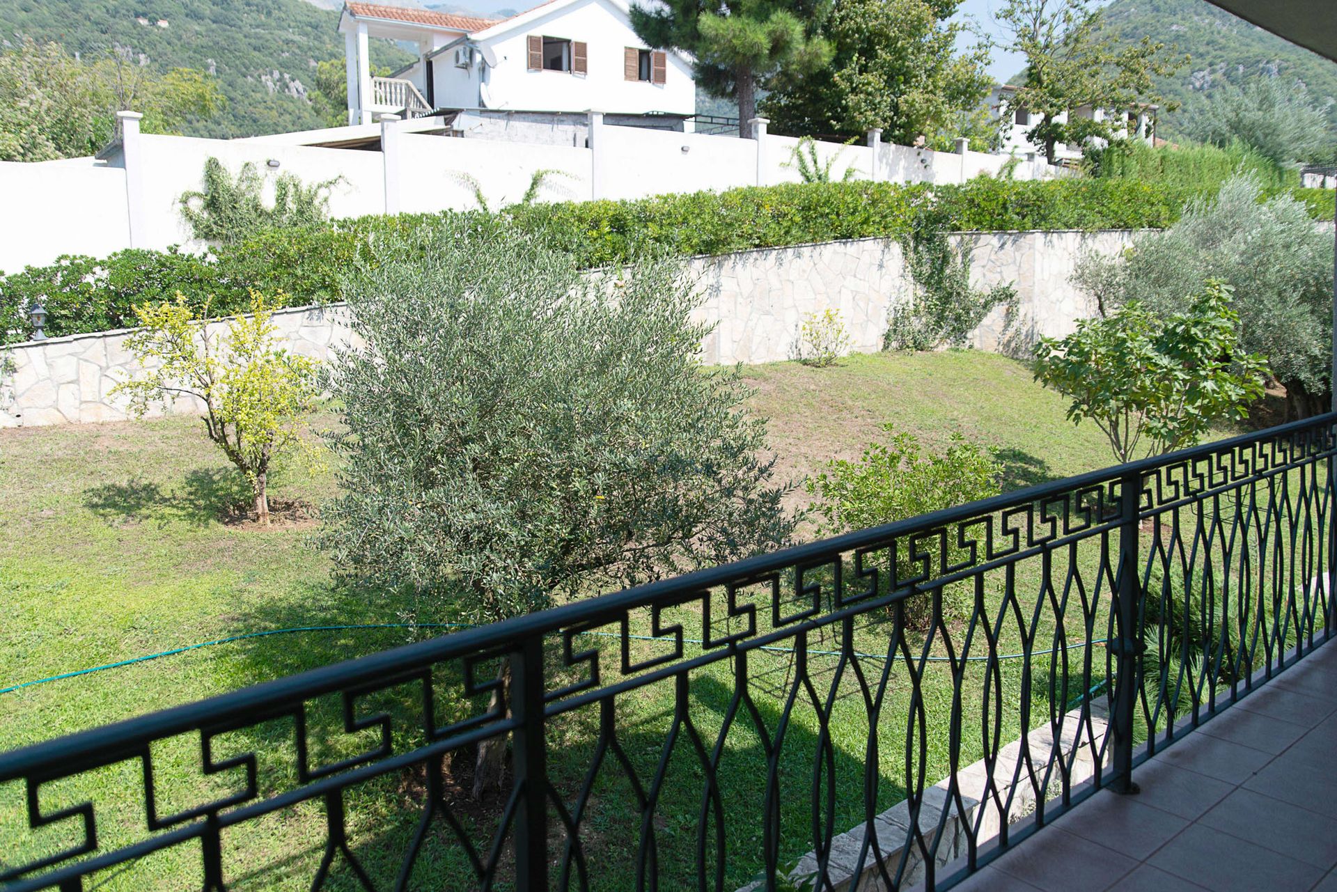 View from the townhouse balcony in Lastva, Montenegro: a green garden with olive trees and a wrought-iron terrace railing.