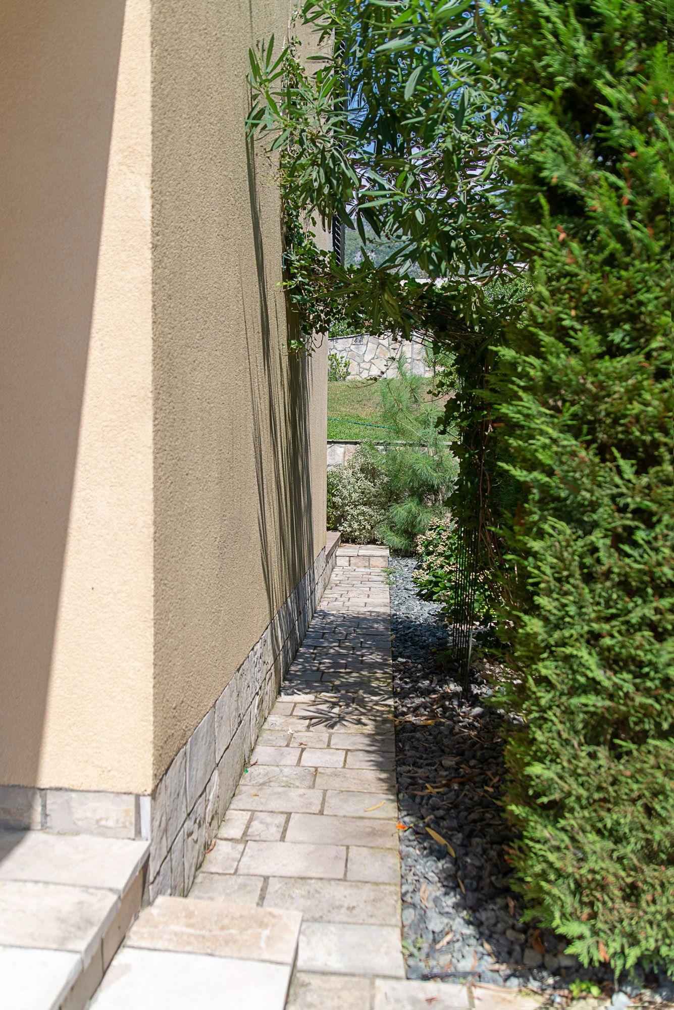 Well-maintained garden path along the house wall in Lastva, Montenegro, with ornamental plants and landscaping.
