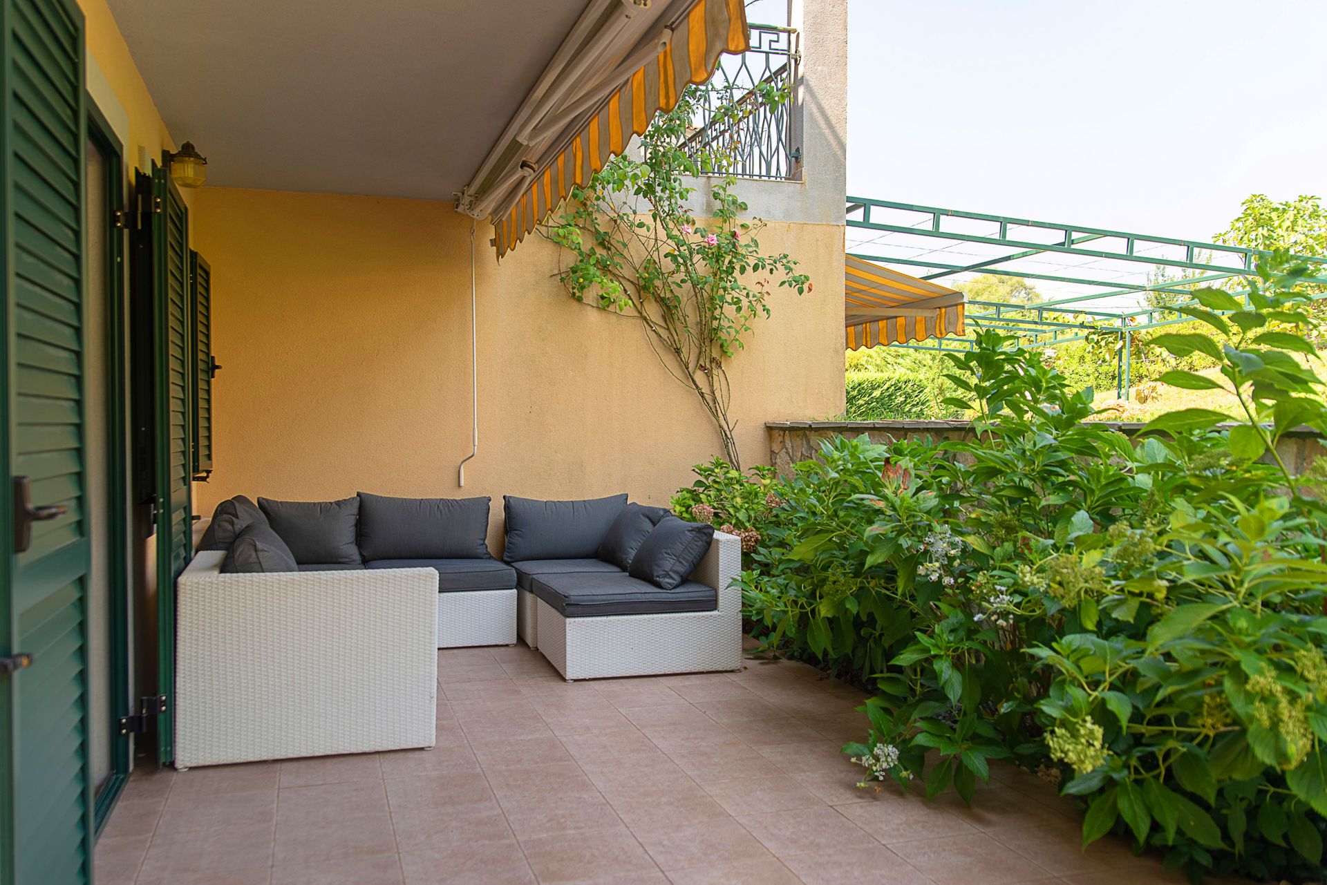 Cozy terrace with wicker furniture and a garden in a townhouse, Lastva, Montenegro. Sunny balcony with an awning and greenery.