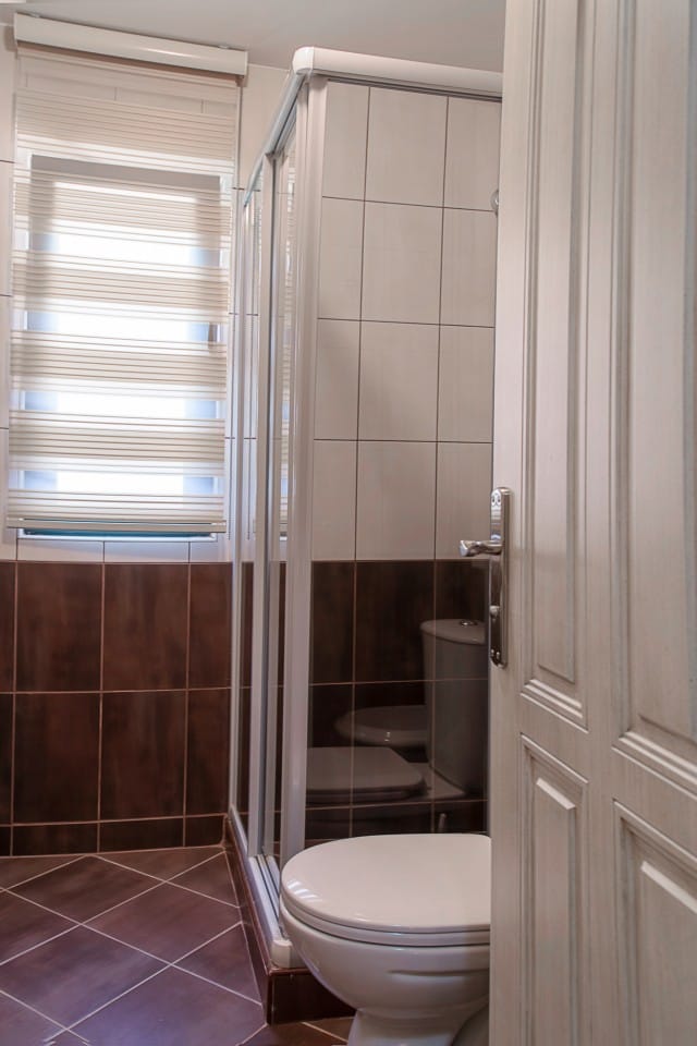 Bathroom in a townhouse in Lastva, Montenegro: shower cabin, light-colored tiles, and a window with blinds.