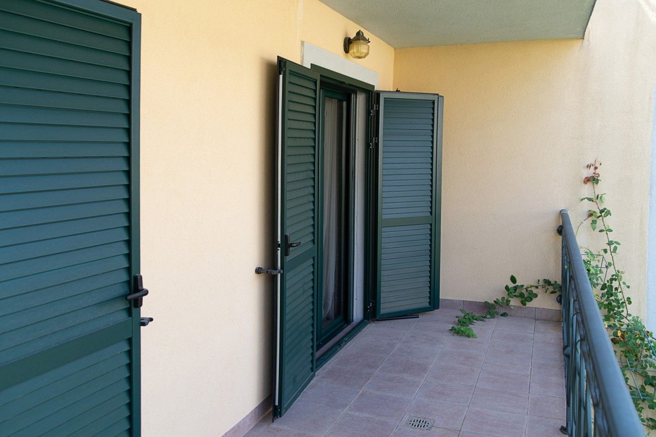 Townhouse balcony in Lastva, Montenegro: tiled floor, green shutters on the doors, and a wrought-iron railing with plants.