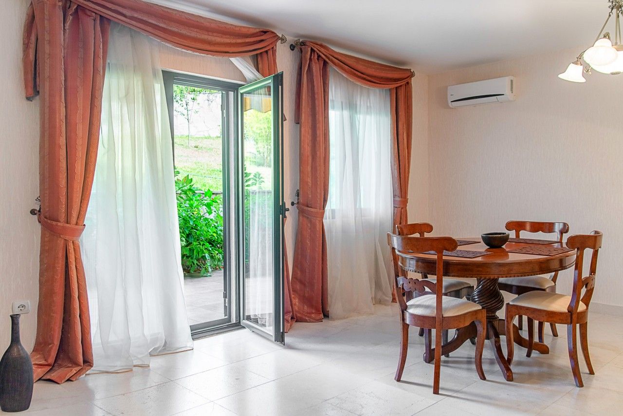 Living room with dining area and access to the terrace in a townhouse, Lastva, Montenegro: wooden table, light flooring.