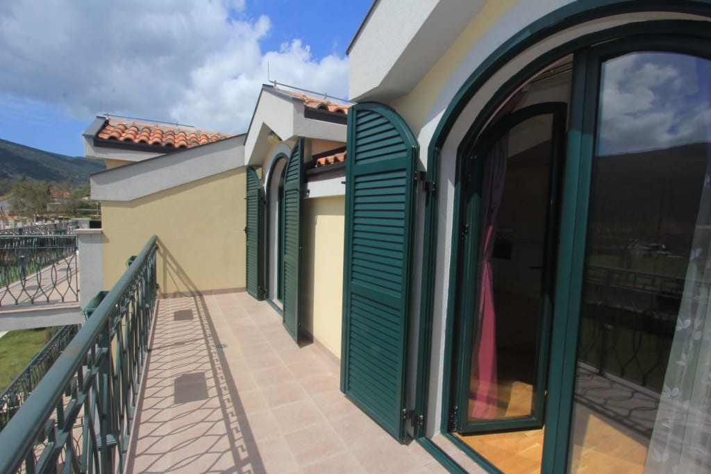 Spacious townhouse balcony in Lastva, Montenegro, with green shutters, wrought-iron railings, and mountain views.
