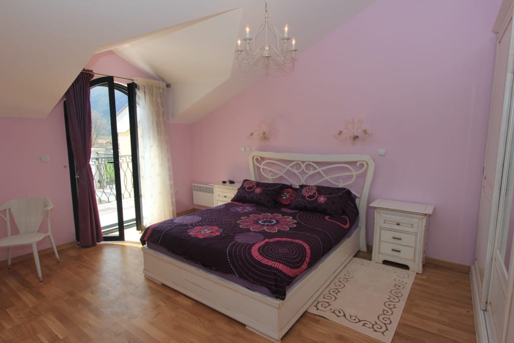 Cozy bedroom in a townhouse in Lastva, Montenegro: a double bed, light-colored furniture, and access to a balcony with a view.