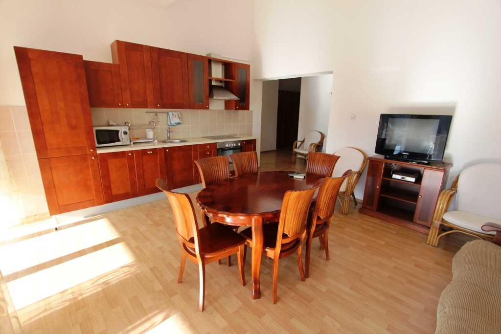 Living room with kitchen in a mini-hotel, Sutomore, Montenegro: wooden dining set, kitchenette, and TV area.