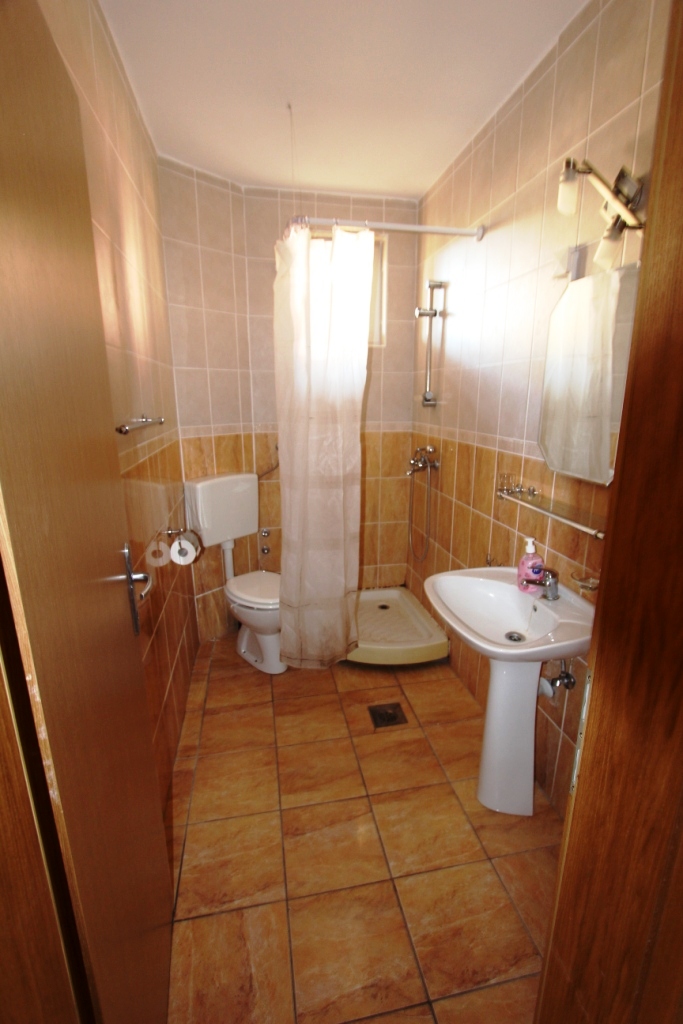 Bathroom with a shower cabin and white fixtures in a mini-hotel, Sutomore, Montenegro. Beige tile finish.