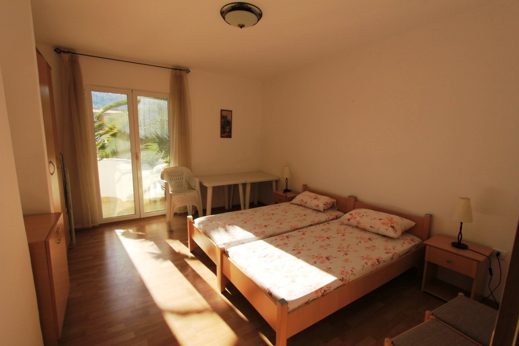Bright bedroom with two beds in a mini-hotel, Sutomore, Montenegro: view of the terrace and light wood furniture.
