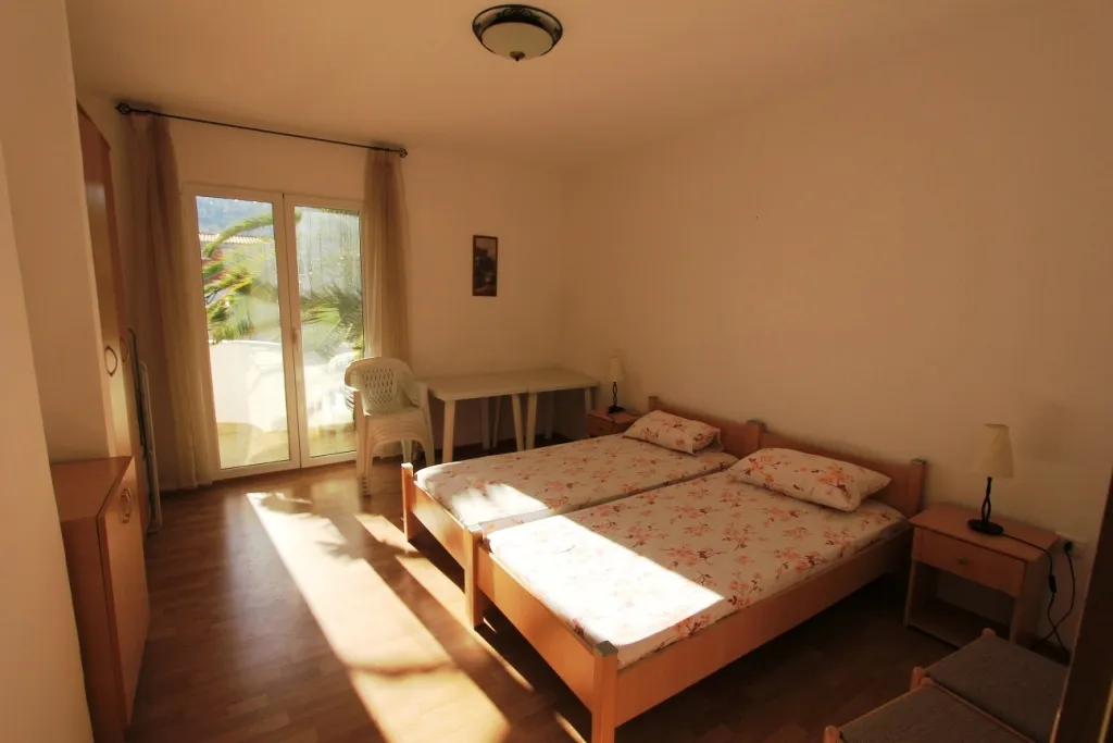 Two single beds with floral bedding, wooden floor, wardrobe, and glass door leading to a balcony.