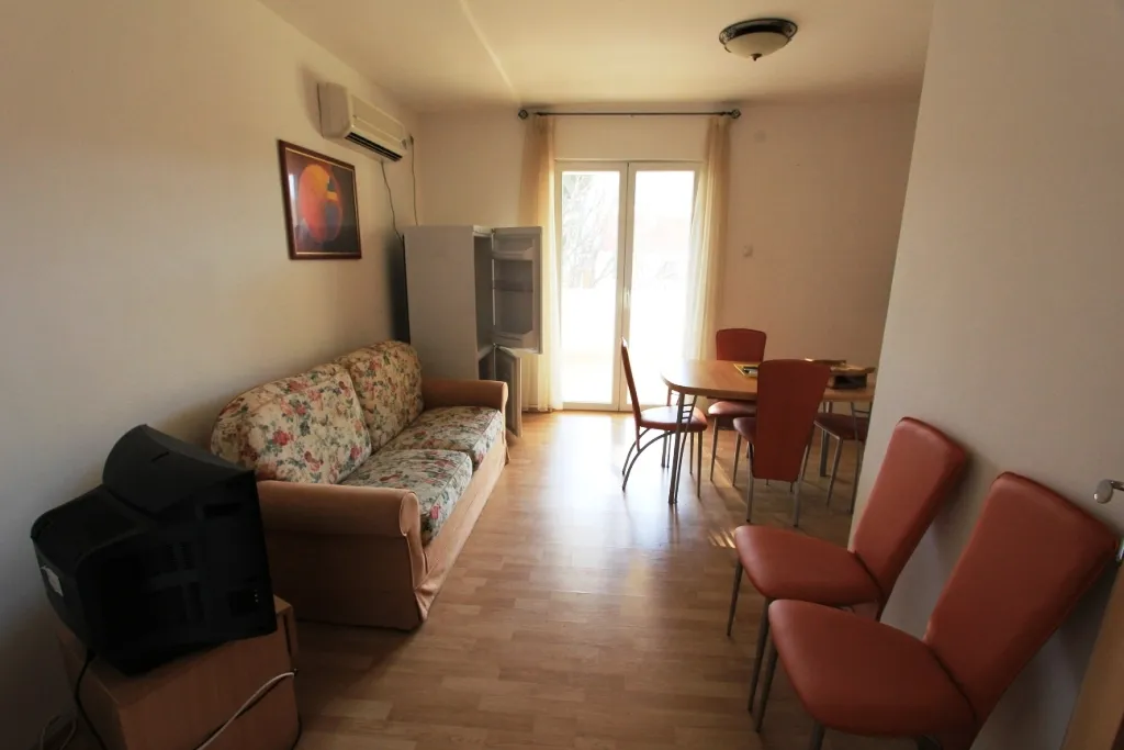 Living room with floral sofa, old TV, dining table, and open fridge near glass doors.
