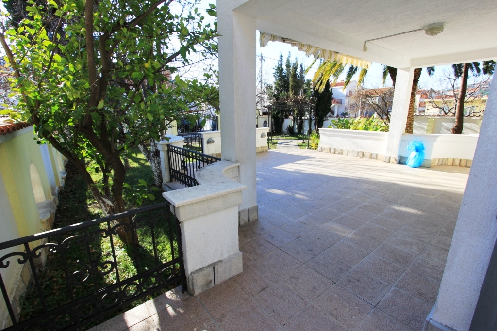 Spacious terrace with tiled flooring and wrought-iron railing at a mini-hotel in Sutomore, Montenegro, overlooking a green garden and trees.