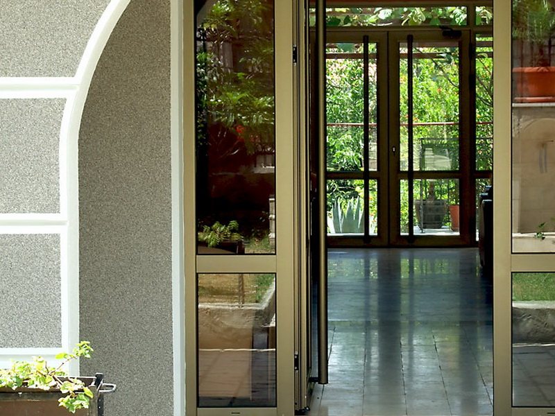 Hotel entrance in Petrovac, Montenegro: glass doors, a terrace with a garden, and stone facade detailing.