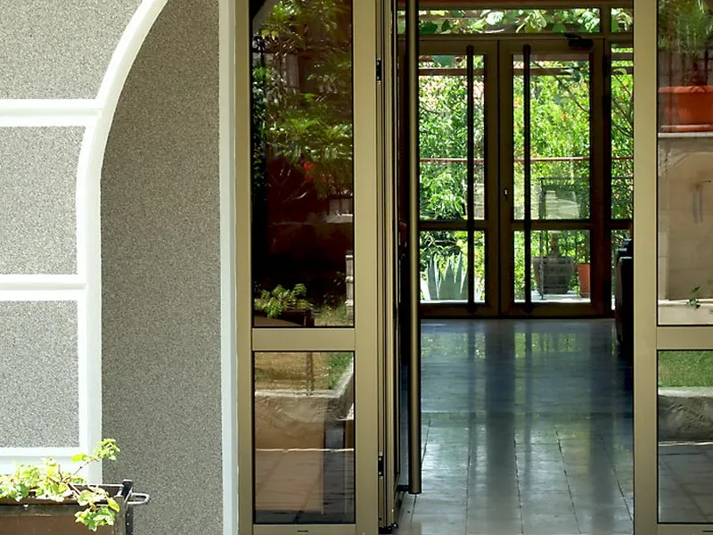 View of glass doors and a dark-floored corridor leading to a garden. Part of an exterior wall is visible on the left.