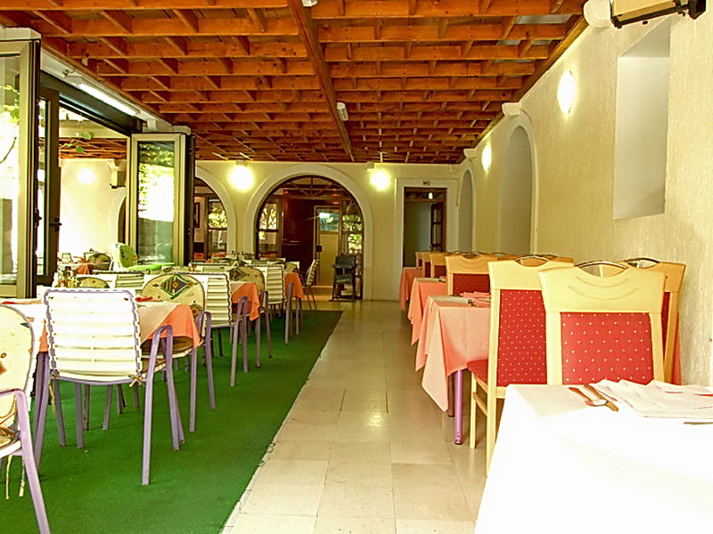 Hotel restaurant interior in Petrovac, Montenegro: covered terrace with a wooden ceiling, tables and chairs for guests.
