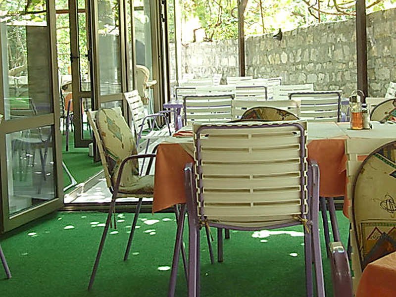 Summer terrace of a hotel in Petrovac, Montenegro: tables with orange tablecloths and plastic chairs outdoors.