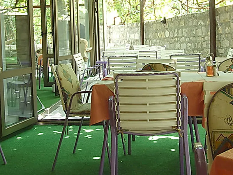 Terrace with dining tables and plastic chairs on artificial grass next to a stone wall.