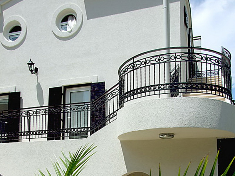 Hotel facade in Petrovac, Montenegro: white walls, round windows, and wrought-iron railings on the building terrace.