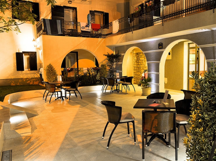 Evening hotel terrace in Petrovac, Montenegro: a cozy lounge area with wicker furniture and arched building openings.
