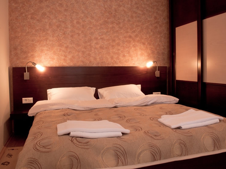 Cozy bedroom with a double bed at the Petrovac hotel, Montenegro: dark furniture, wall sconces, and decor.
