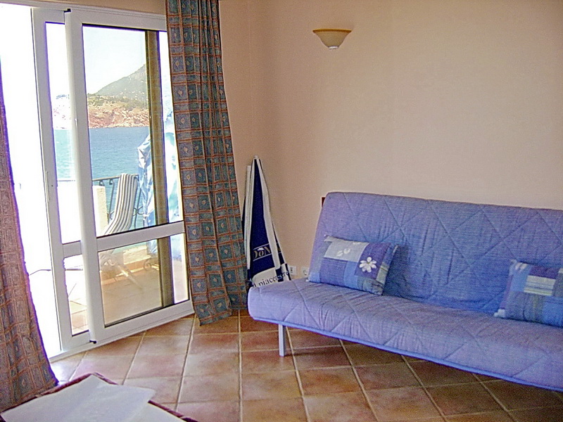 Living room in a hotel in Sutomore, Montenegro: blue sofa, tiled floor, and panoramic sea view from the terrace.