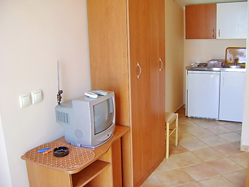 Hotel room interior in Sutomore, Montenegro: compact kitchen, wooden wardrobe, and TV on a stand.