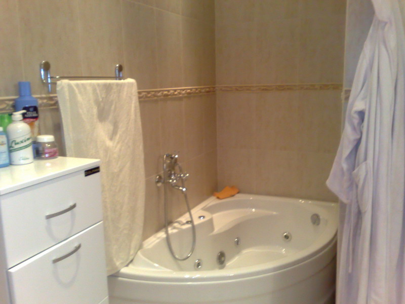 Bathroom with a corner whirlpool tub in a house, Sutomore, Montenegro: white furniture and beige tiles.