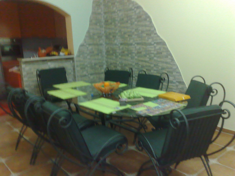 Dining area in the living room of a house in Sutomore, Montenegro: glass table, wrought-iron chairs, and walls finished with decorative stone.