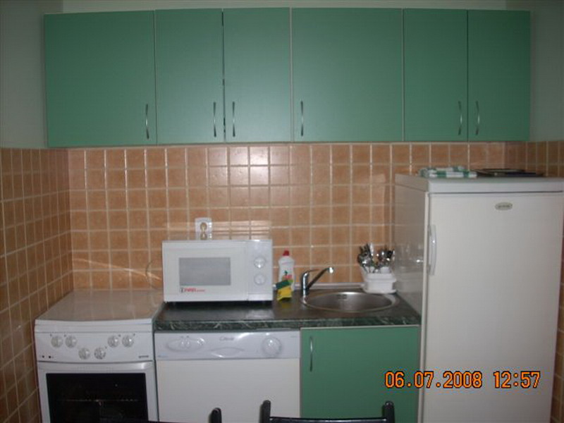 Compact kitchen with green cabinet fronts, a stove, a refrigerator, and beige tile in a house, Sutomore, Montenegro.