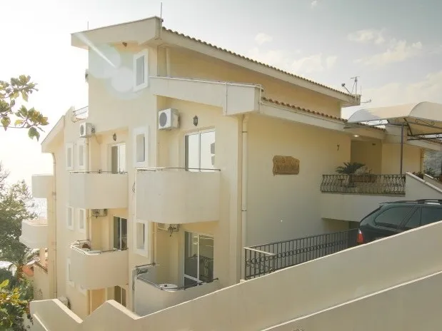 Exterior view of a multi-story residential building featuring balconies, AC units, and a parked car.