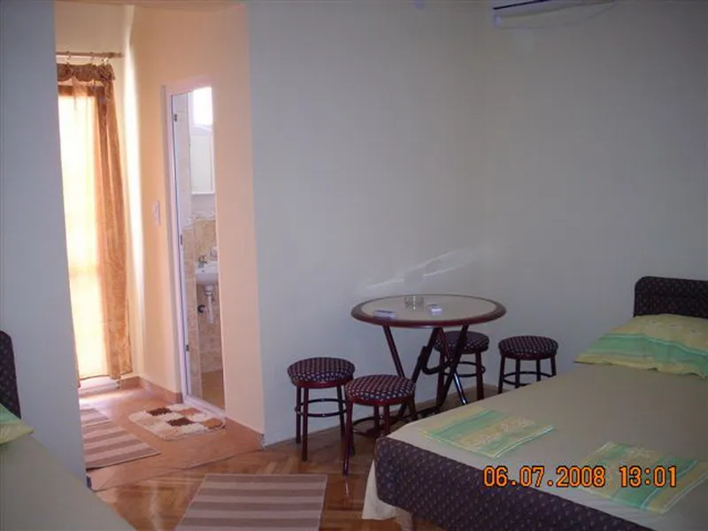 Room with a bed, small round table and stools. Doorway to bathroom visible, plus window with curtains.