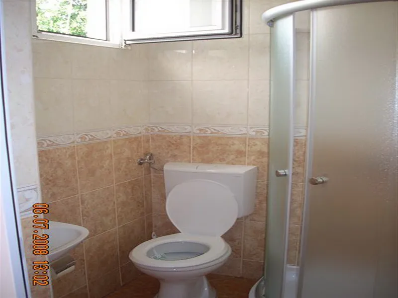 Bathroom featuring a white toilet, corner shower cabin, and sink against beige tiled walls with a decorative border.