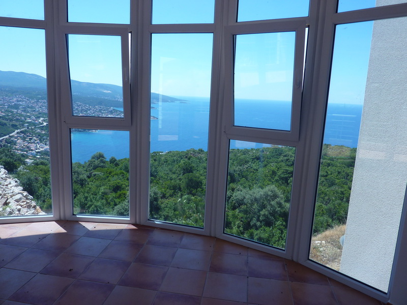 Panoramic view of the sea and mountains from the villa’s living room in Dobra Voda, Montenegro, with access to a terrace with tiled flooring.