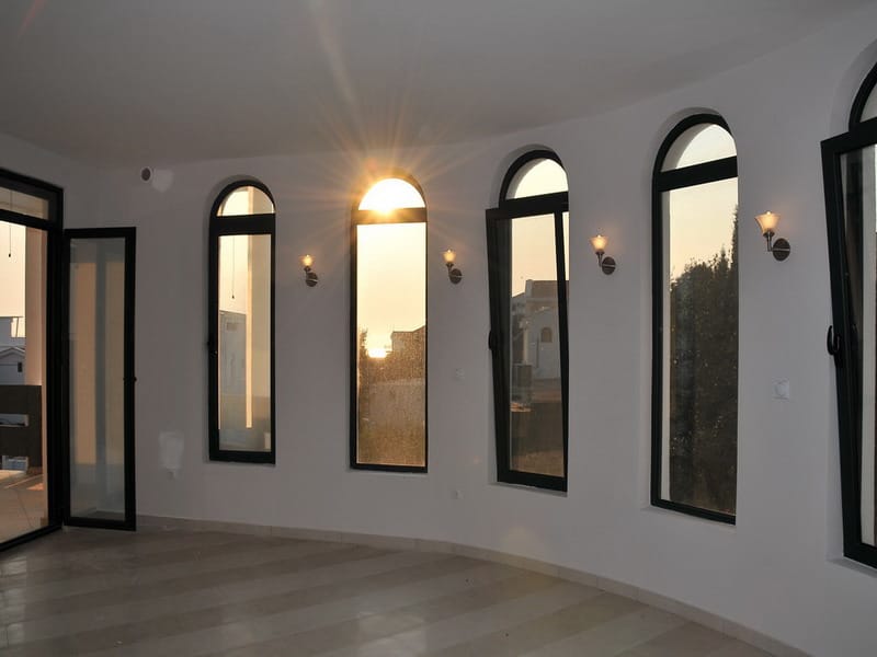 Bright living room with arched windows and sunset views in a house, Uteha, Montenegro. Modern interior with white finishes.
