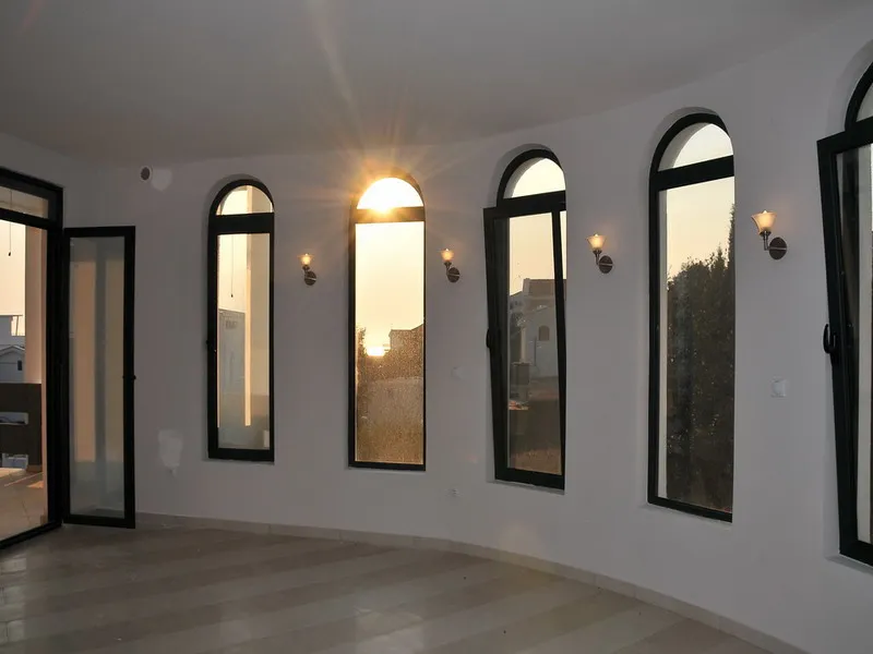 Empty room with arched windows and polished floor, illuminated by setting sun through glass.