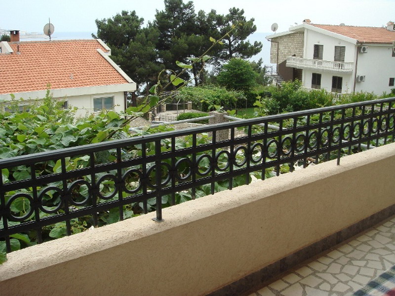 View from the balcony of a house in Bar, Montenegro: wrought-iron railing, a terrace with a stone floor, and a view of a green garden.