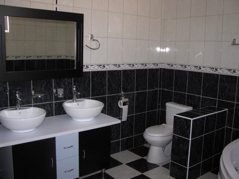 Bathroom in a house in Utjeha, Montenegro: black-and-white tile, two sinks on a vanity, and a mirror in a black frame.