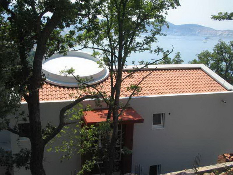 Modern house with a tiled roof and sea view in Shushan, Montenegro, surrounded by greenery and trees.
