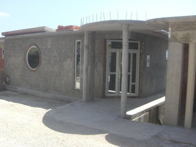 House under construction in Shushan, Montenegro: facade with a round window, concrete columns, and installed double-glazed windows.