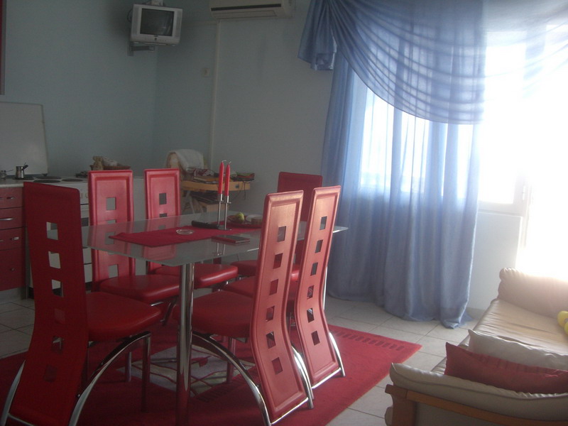 Living room with dining area in a house, Shushan, Montenegro: glass table, red chairs, and light curtains.