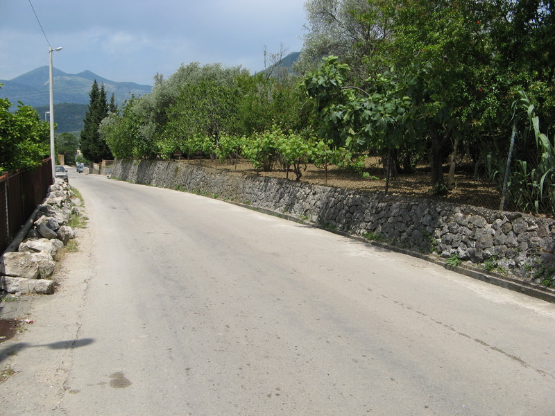Paved road along the plot with a stone fence and garden in Bar, Montenegro.
