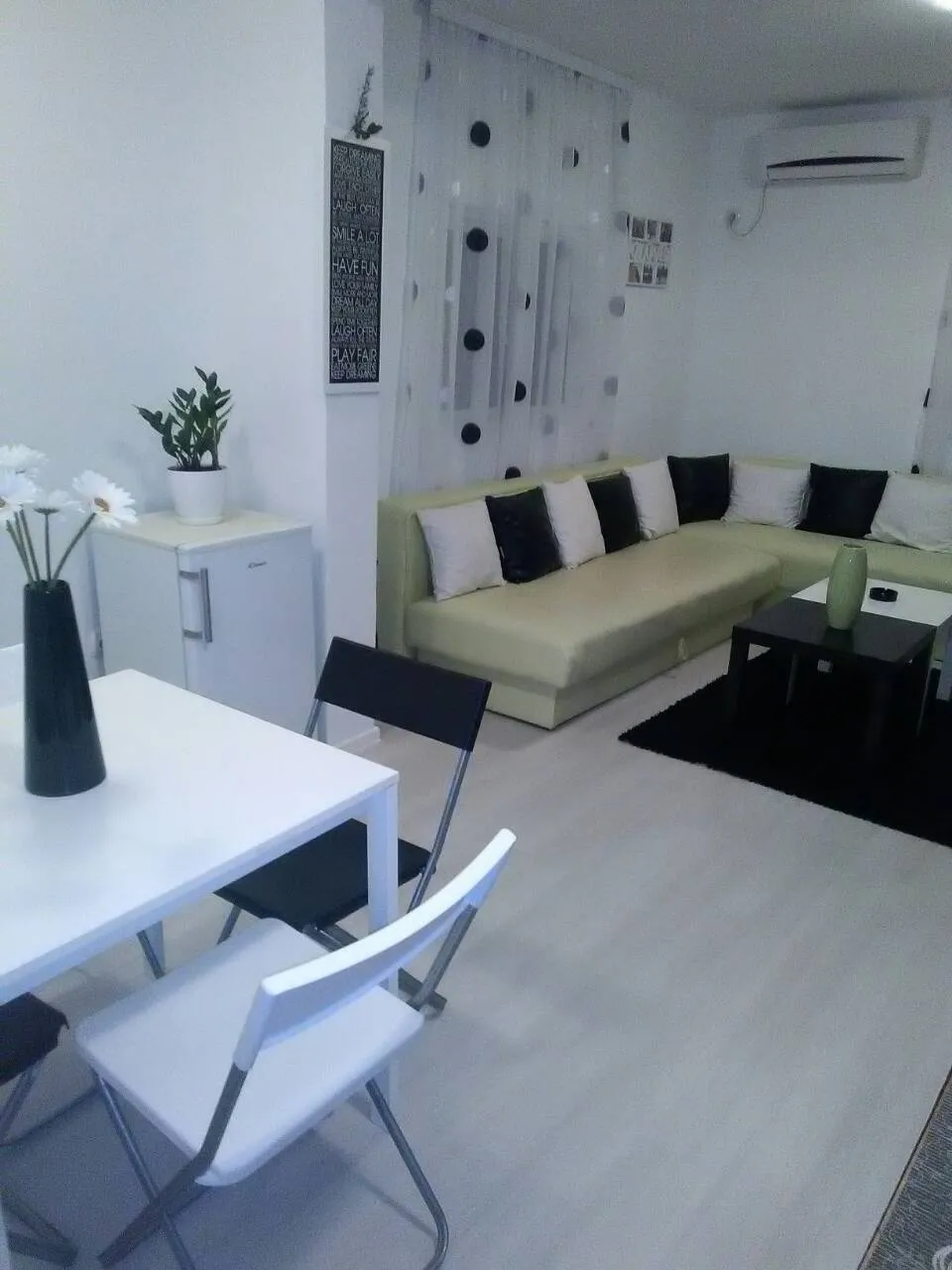 Living room featuring a corner sofa, white dining table, black coffee table, and wall-mounted air conditioner.
