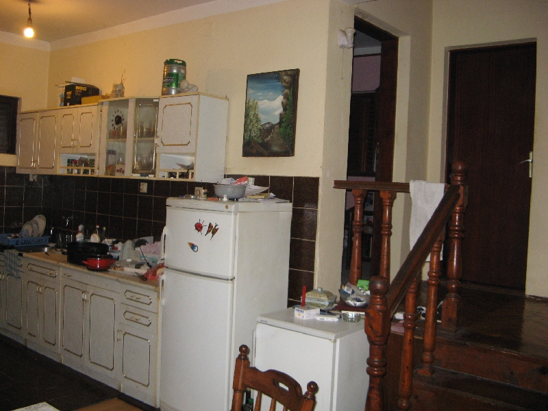 Kitchen in a house in Shushan, Montenegro: light cabinetry, dark backsplash, refrigerator, and a wooden staircase to the second floor.
