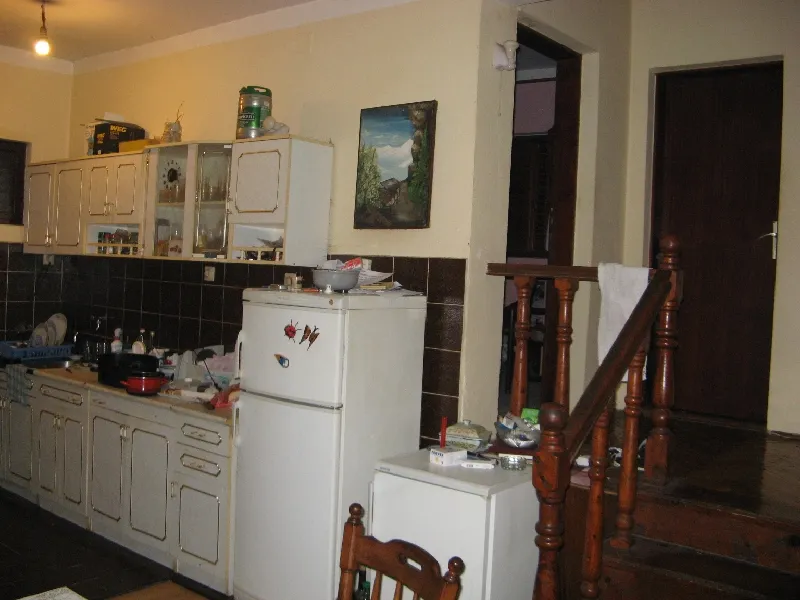 Kitchen with white cabinets, refrigerator, dark tile backsplash, and wooden staircase visible on the right.