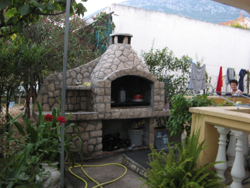 Stone barbecue grill in the garden of a private house in Shushan, Montenegro, with mountain views and a terrace with a balustrade.