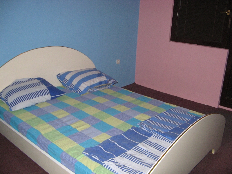 Bedroom with a double bed in a house, Shushan, Montenegro: bright walls, plaid bedding, and dark flooring.