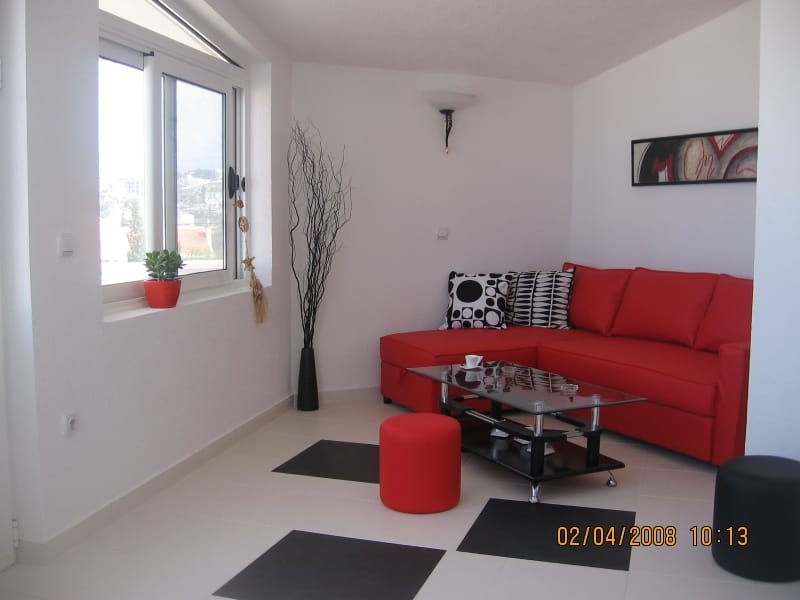 Living room with a red sofa and glass table in a house in Utjeha, Montenegro, a bright interior with a view from the window.